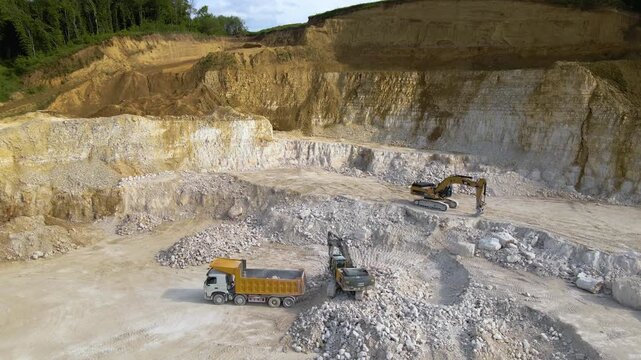 Open pit mining of construction sand stone materials with excavators and dump trucks.