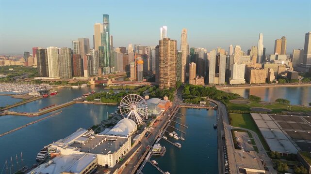 Stunning aerial drone footage of Chicago downtown skyline featuring Navy Pier with its iconic ferris wheel and Lake Michigan harbor. Golden sunrise light illuminates skyscrapers and marina boats.