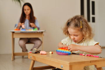 Naklejka premium A child sits at a table creating a shape with modeling clay while an adult is at a nearby table using craft supplies in a home setting during the afternoon