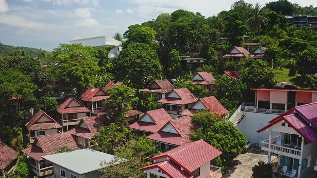 Tropical resort accommodations lining a lush green hillside, traditional Thai style bungalows and modern villas, offering a serene vacation, travel escape in Phuket, Thailand. Aerial view drone flight