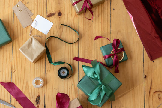 Large green gift sitting centered on light wooden table surrounded by ribbons, tags, tape