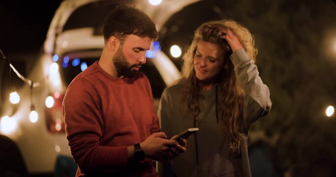 Couple enjoys time together under string lights while sharing moments with a phone in their outdoor setup at night