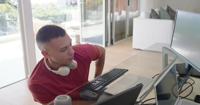 African American man leaning toward stacked keyboard, adjusting, typing to start work at glass desk