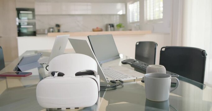 Camera is moving closer, causing VR headset to grow on table beside laptop, highlighting workspace