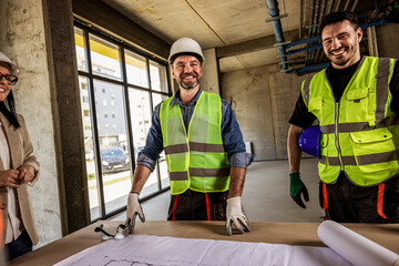 Naklejka premium Construction crew and female architect talking around a table with blueprints.