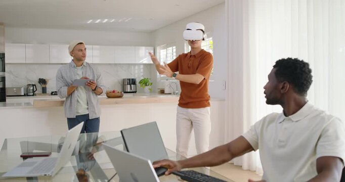 Diverse team seeing standing man in rust polo picking white VR headset, showing controls in kitchen