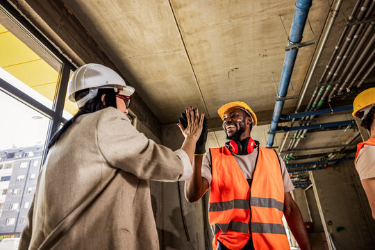 Diverse construction team celebrating with a high five during site meeting.