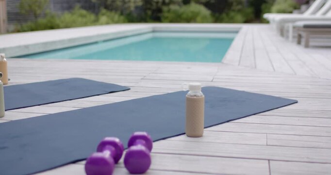 Sunlight is warming wooden deck and sparkling pool, yoga mats and dumbbells are awaiting practice