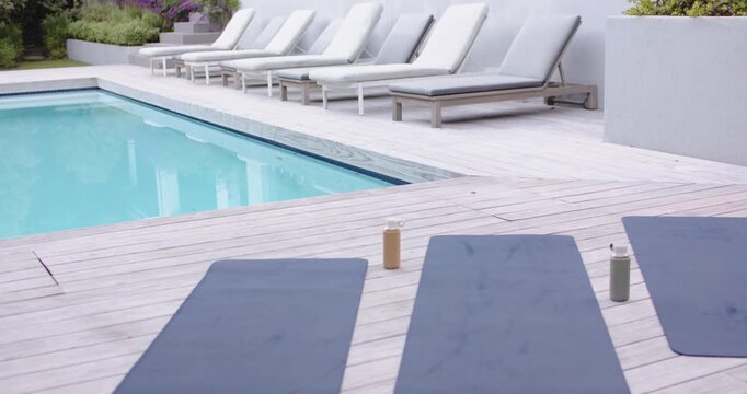 Camera is pulling back, revealing three dark blue mats on pool deck for morning workout