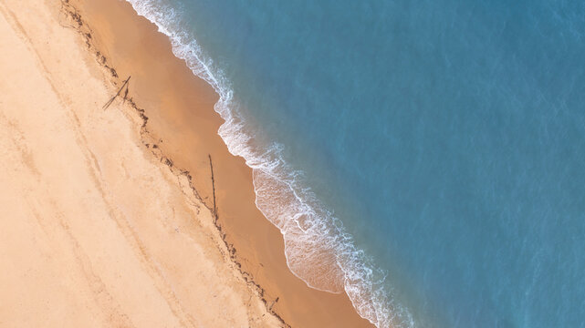 Aerial view of ocean waves gently touching sandy beach shoreline creating a calm coastal pattern. Perfect natural background for tourism promotions, summer visuals, and relaxation themes.