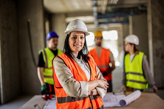 Smiling female construction worker in safety gear with crew working in background.