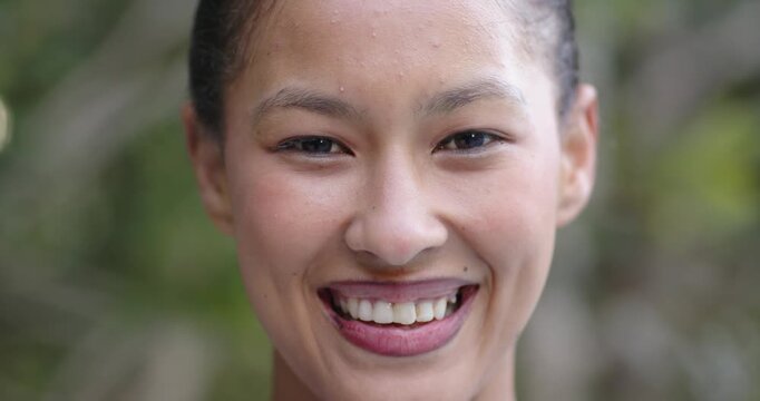 African American woman smiling, parting lips and laughing in shaded garden with forehead droplets
