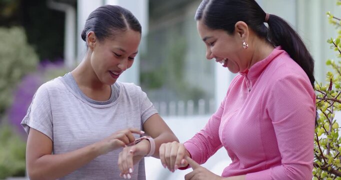 Diverse female friends holding wrist up checking band pointing tapping screen and laughing on porch
