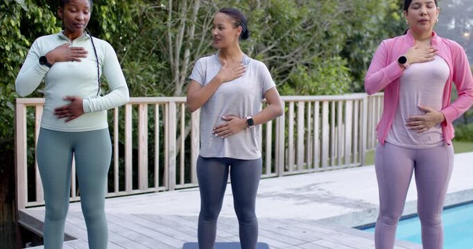 Three women breathing following instructor placing hands on chest belly on yoga mats on wooden deck