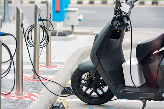 Electric scooter plugged into charging station at urban parking lot