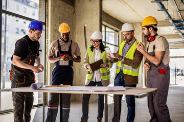 Construction workers and architects collaborating around a table with a digital tablet and building...
