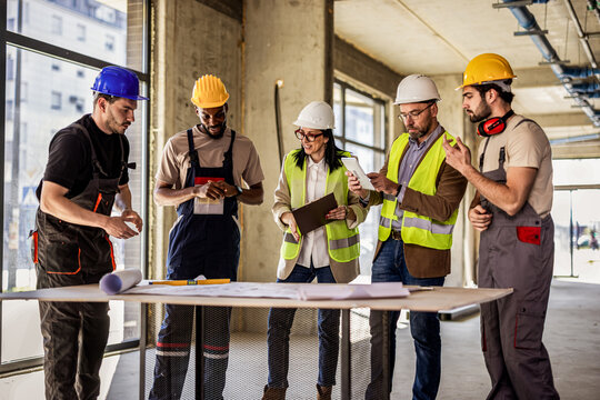Construction workers and architects collaborating around a table with a digital tablet and building plans.