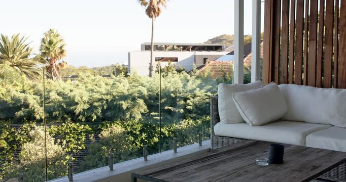 Camera is panning right on terrace as shot starts, passing wicker sofa and table, revealing ocean