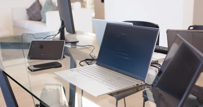 Camera panning slightly right, open laptop showing text on glass table, revealing reflections