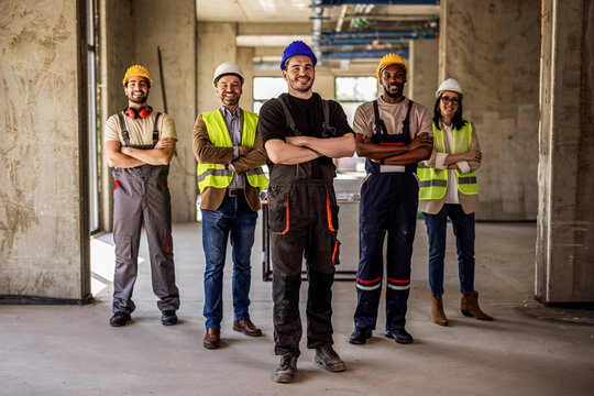 Smiling builder posing with arms crossed alongside a diverse architectural team.
