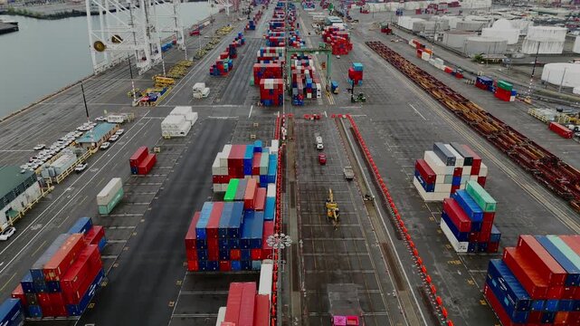Aerial drone reverse flight over container port with stacked shipping containers and cargo cranes