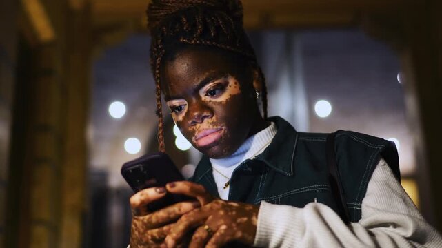 Smiling young woman vitiligo skin typing smartphone screen close up outdoors. Happy female student laughing reading funny text notification browsing social media content network app
