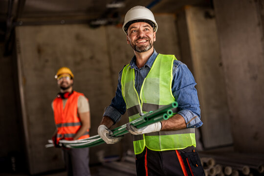 Two builders holding small green pipes on an industrial renovation site.