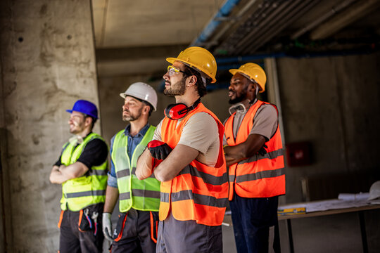 Four construction workers with folded arms looking through a window on site.