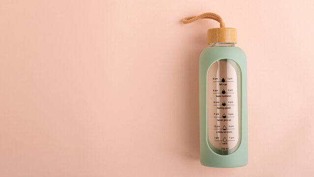 Reusable glass water bottle tracking daily hydration on pink background