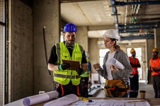Two construction workers analyzing blueprints to organize workflow on site.