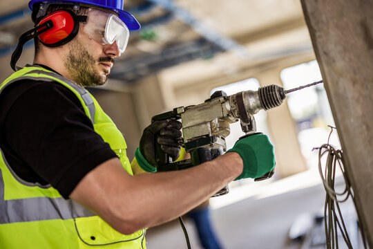 A construction worker using a handheld hammer drill on a brick wall.