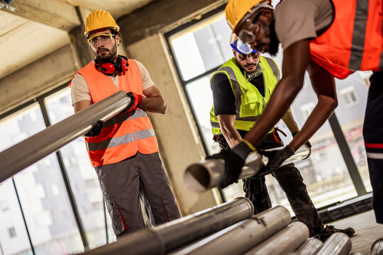 A diverse construction crew lifting heavy industrial pipes on a renovation site.