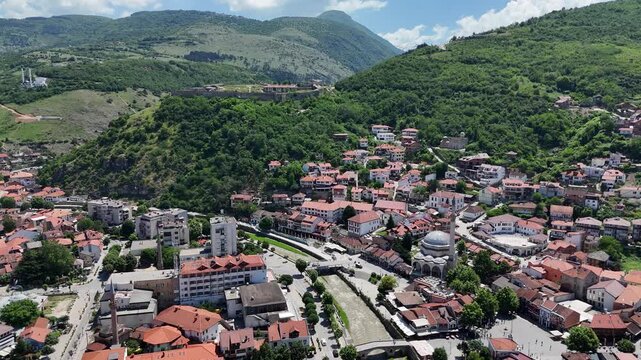 Aerial drone footage of Prizren city and its historic fortress captured on a clear sunny day, highlighting the beautiful blend of traditional architecture, urban life, and the famous hilltop castle ov