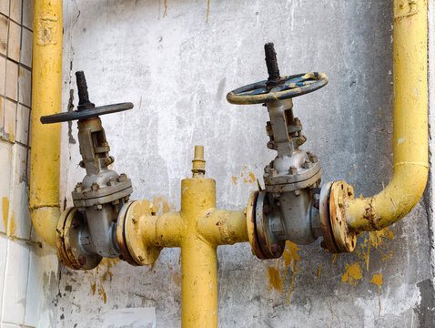 Gas pipeline valves mounted on the outside facade of a residential house with yellow metal pipes and technical engineering communication detail