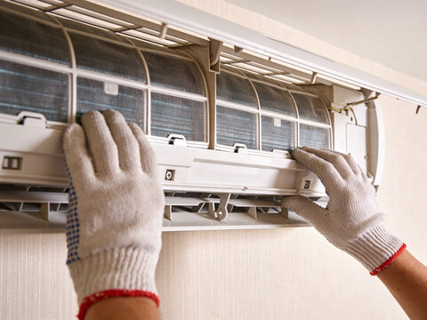 A close-up view of a technician wearing gloves performing maintenance on a wall mounted air conditioner.