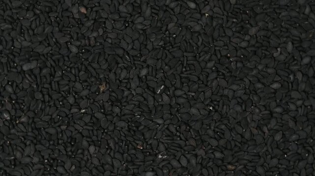 Top view macro shot of a heap of raw organic black sesame seeds rotating slowly. High quality background texture.
