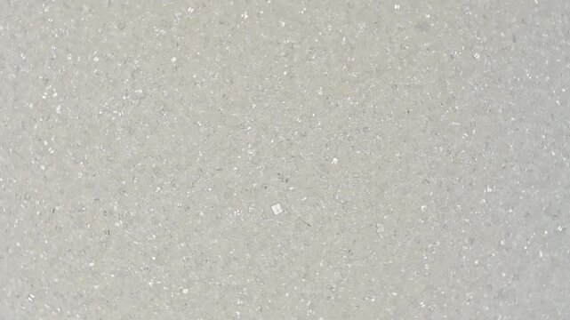 Top view macro shot of white refined sugar crystals rotating slowly. High quality sweet ingredient texture background