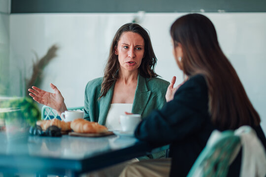 Women arguing in a cafe during a business conflict, experiencing tension and frustration over a disagreement