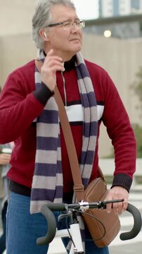 Vertical video: Adjusting earbud, man in red sweater preparing to ride in plaza, holding white bike