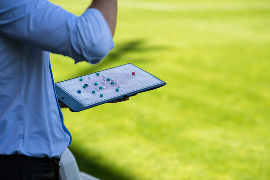A soccer coach holding a tactical clipboard with magnets to plan strategy during a professional football match at a stadium.