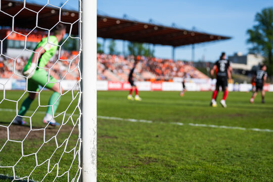 View through a soccer goal net of a goalkeeper in a green kit ready for action during a professional football match.