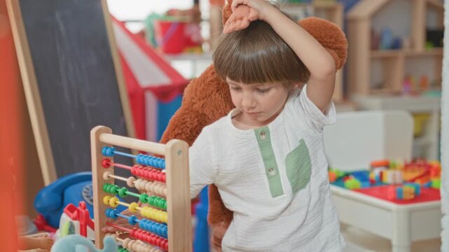 Boy touching abacus beads and holding a plush on his back while concentrating in a preschool classroom activity area; concentration learning.