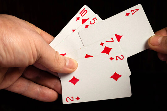 A man holds five playing cards in his hand, ready to play a card game. The action takes place at home in the evening or in a poker club