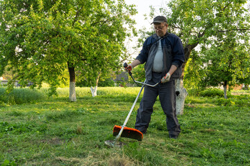 Obraz premium A gardener stands in a backyard trimming grass with a grass trimmer. Trees surround him as he works in bright daylight. The grass is green and the area looks well-kept