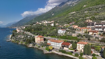 Fototapeta premium Beautiful Italian village captured by drone at sunset over Lake Garda. Peaceful atmosphere with boats on the water and scenic lakeside landscape.