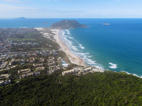 High altitude airplane view of Santinho beach from Morro das Aranhas mountain with resort, urban area, dunes and Badejo island in Florianopolis, Brazil