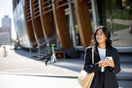 Woman holding phone near modern building in urban setting during daytime