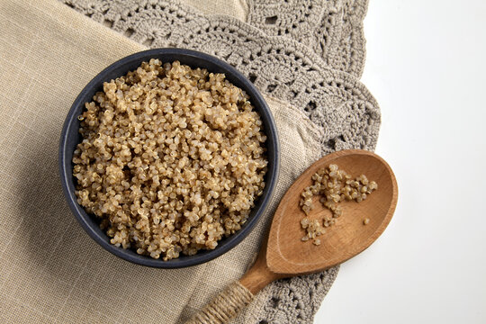 Boiled buckwheat groats in a ceramic bowl and a wooden spoon on a linen tablecloth, top view