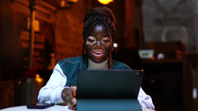 Excited young woman vitiligo skin waving hand tablet computer video call sitting outdoors. Amazed female student laughing genuinely greeting friends online streaming live communication app
