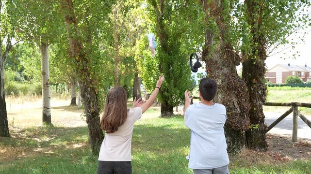 Rear view of a young boy and girl walking in a green park, stopping to throw their headphones in the air and catching them in slow motion